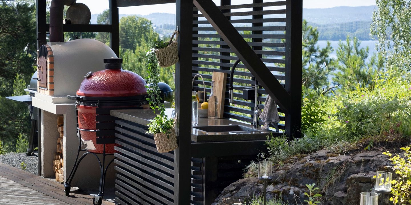 Et utekjøkken beiset i svart og terrassen beiset i brun. I bakgrunnen er det utsikt til sjøen. 