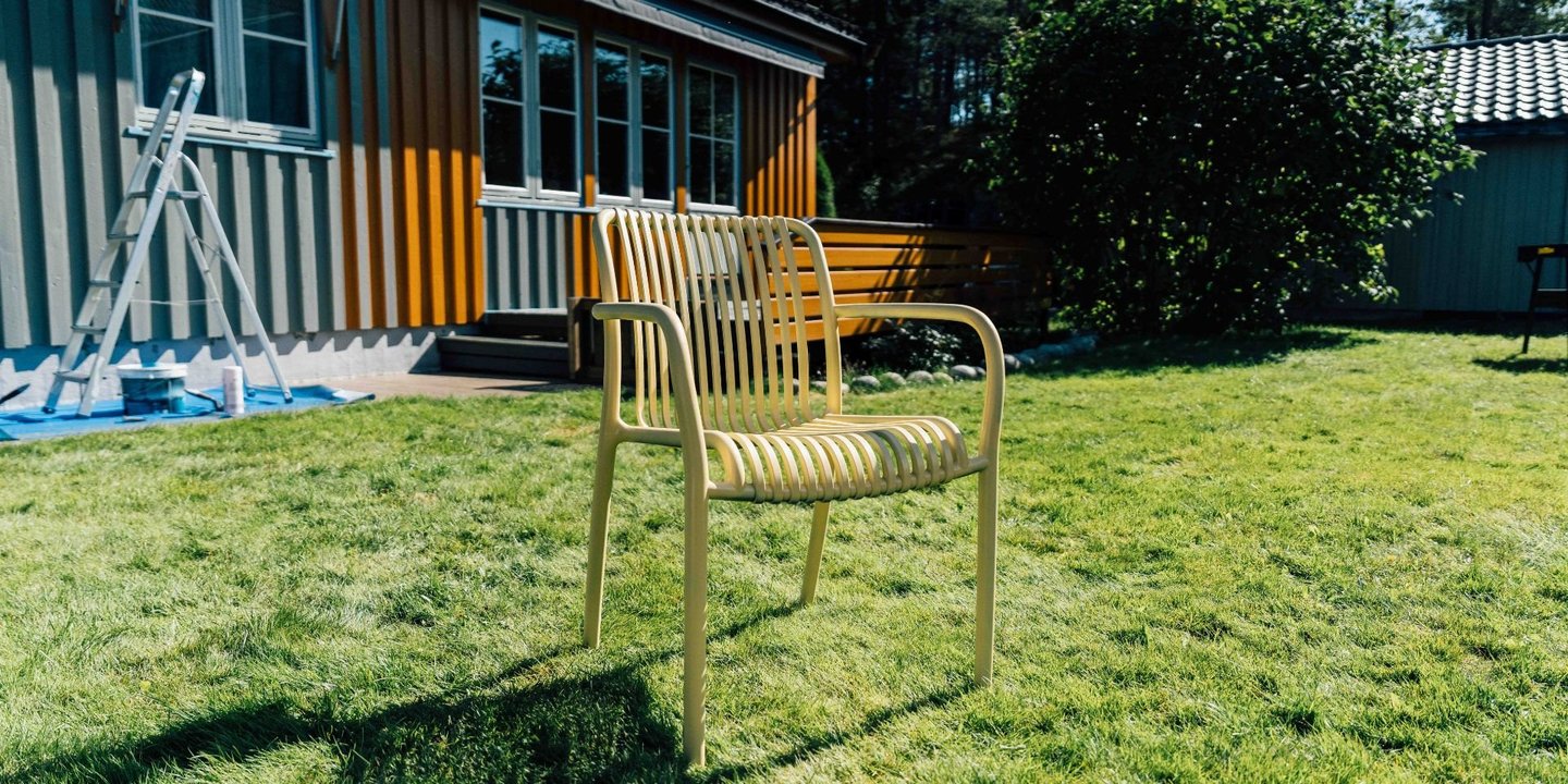 En gul stol står foran et hus på en grønn gressplen i sola