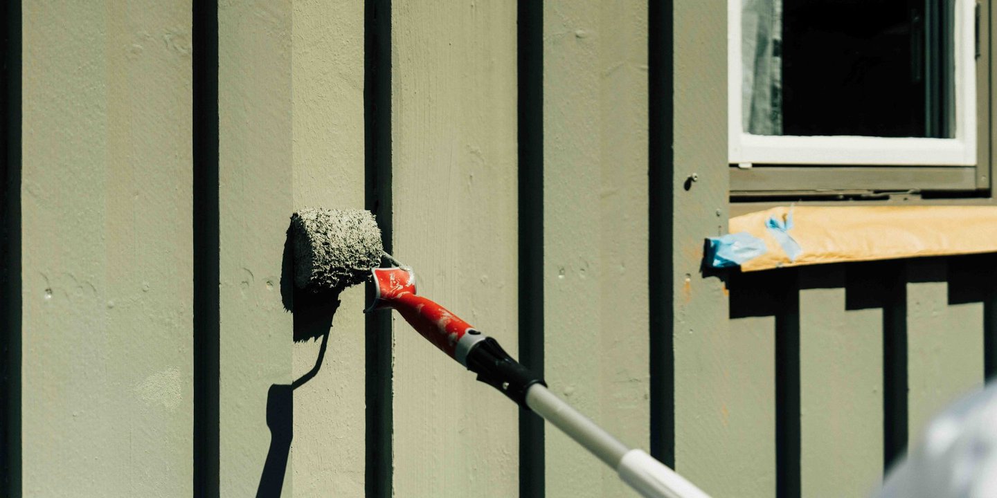 Person bruker en malingsrulle og maler huset grønt