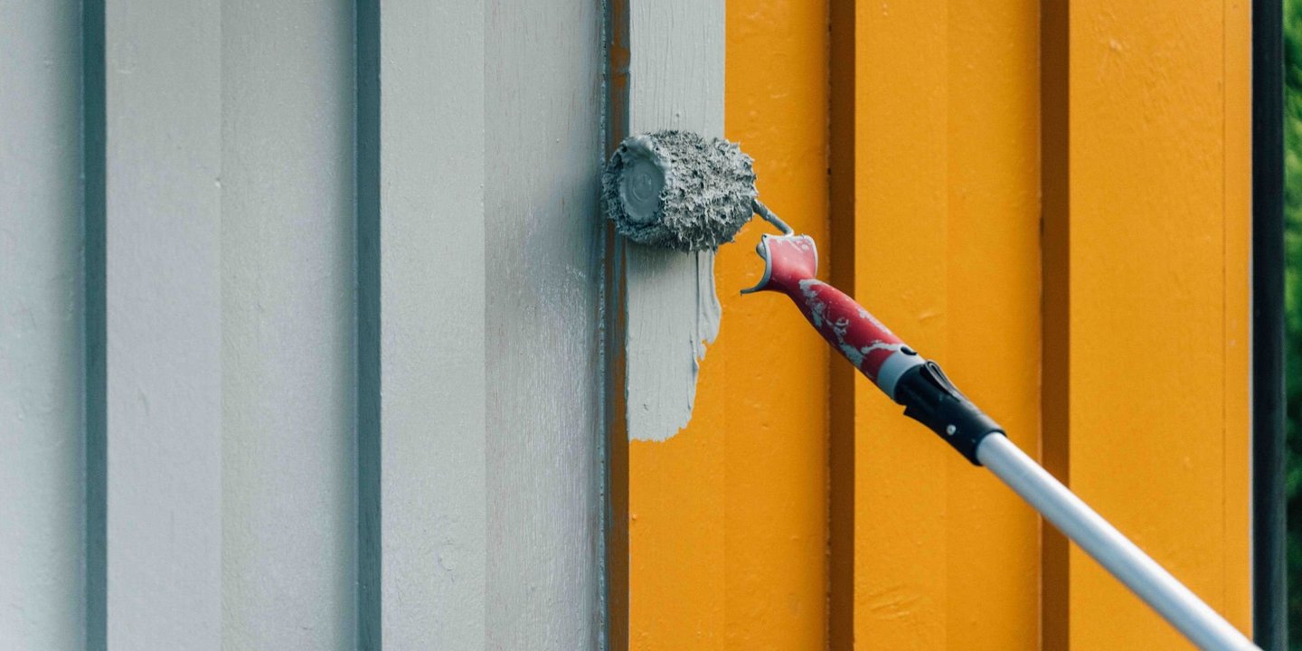 En malingsrulle på forlengerskaft som maler husveggen grå