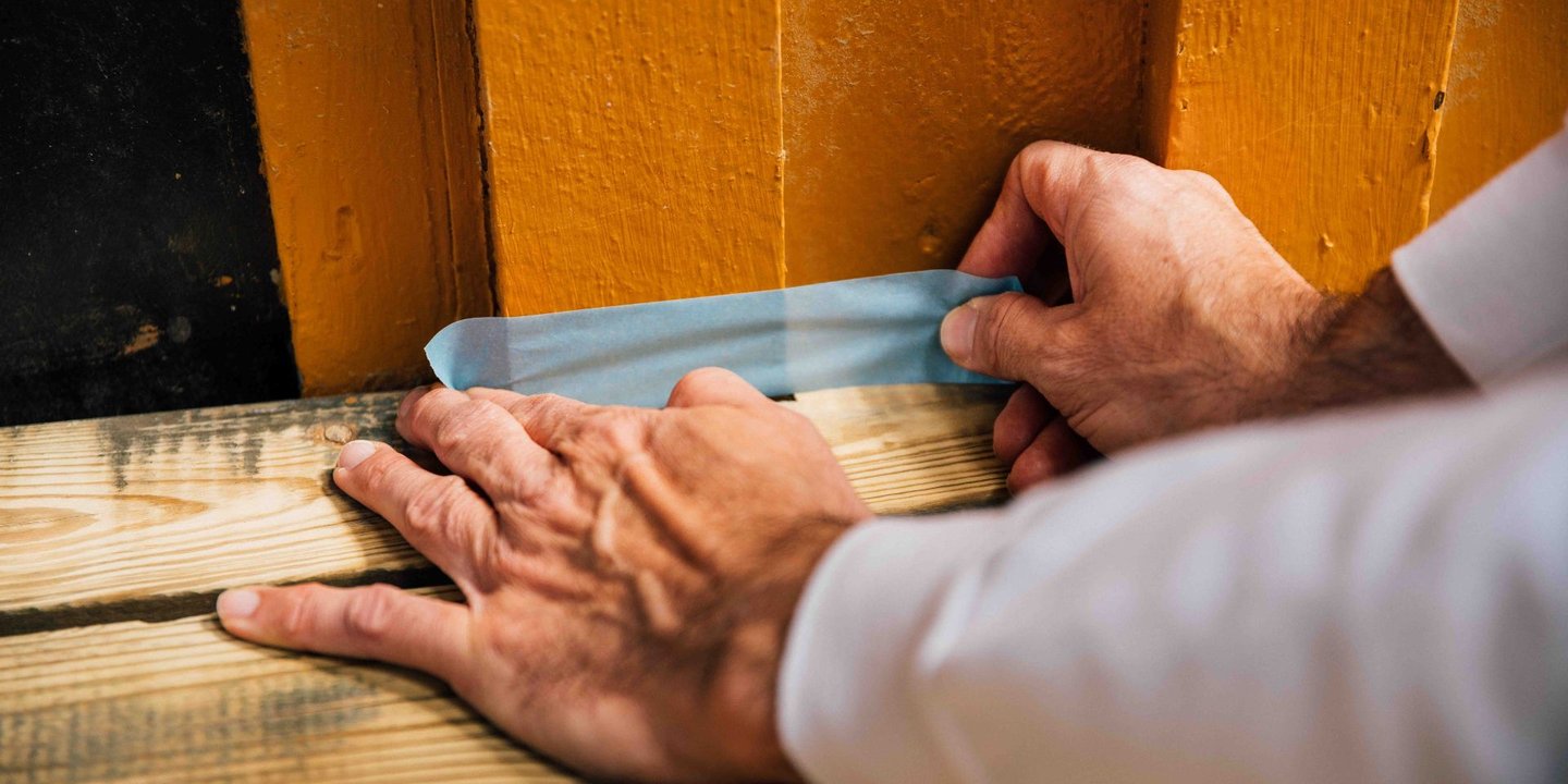 Bilde av hender som jobber med å sette opp maskeringsteip mellom husvegg og terrasse.