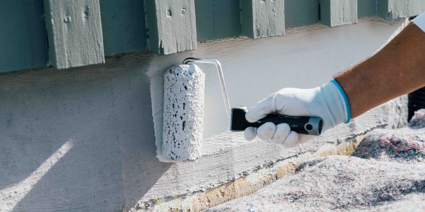 En person med hanske maler grunnmuren med en rulle.