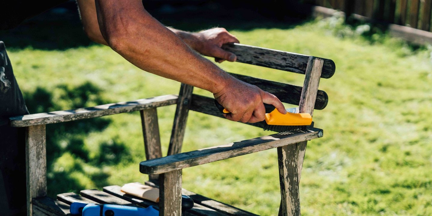 En person forbereder en stol for maling med forarbeid i form av pussing med en kost.