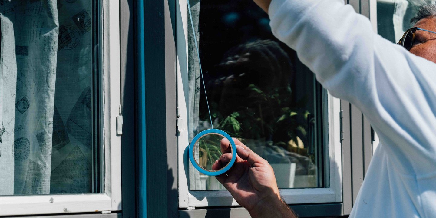 Mann som maskerer et vindu med blå maskeringstape.