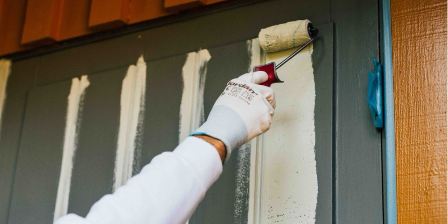 Person bruker malingsrulle for å male en grå dør hvit