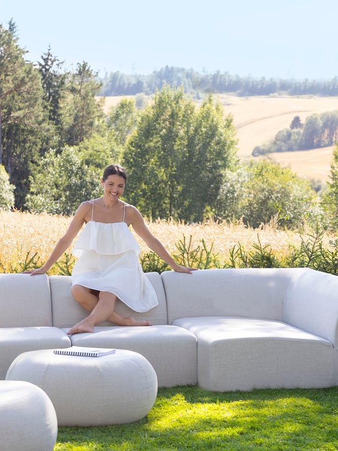 Dame i hvit kjole sitter på en beige Skagen modulsofa. 