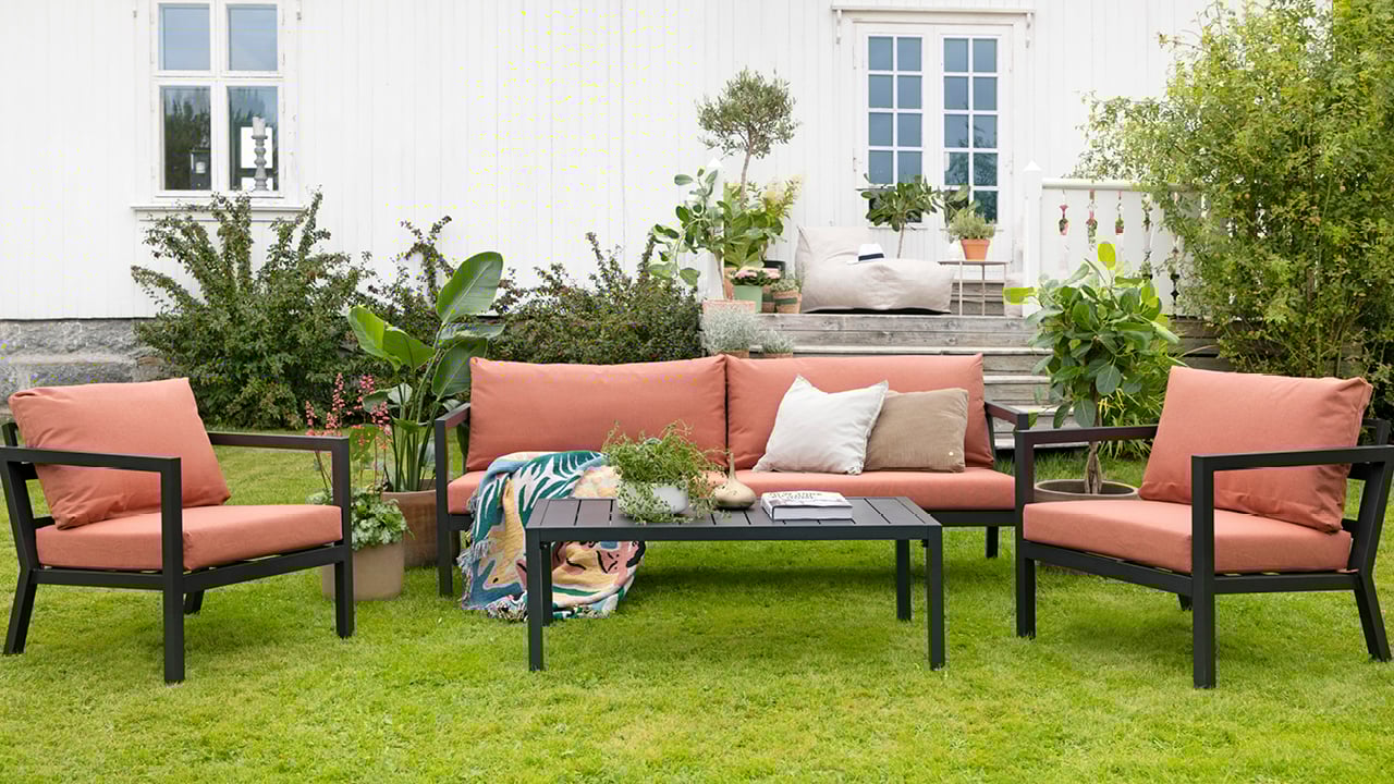 Røst sofaserie, sort med rust, på en grønn gressplen foran et hus. 