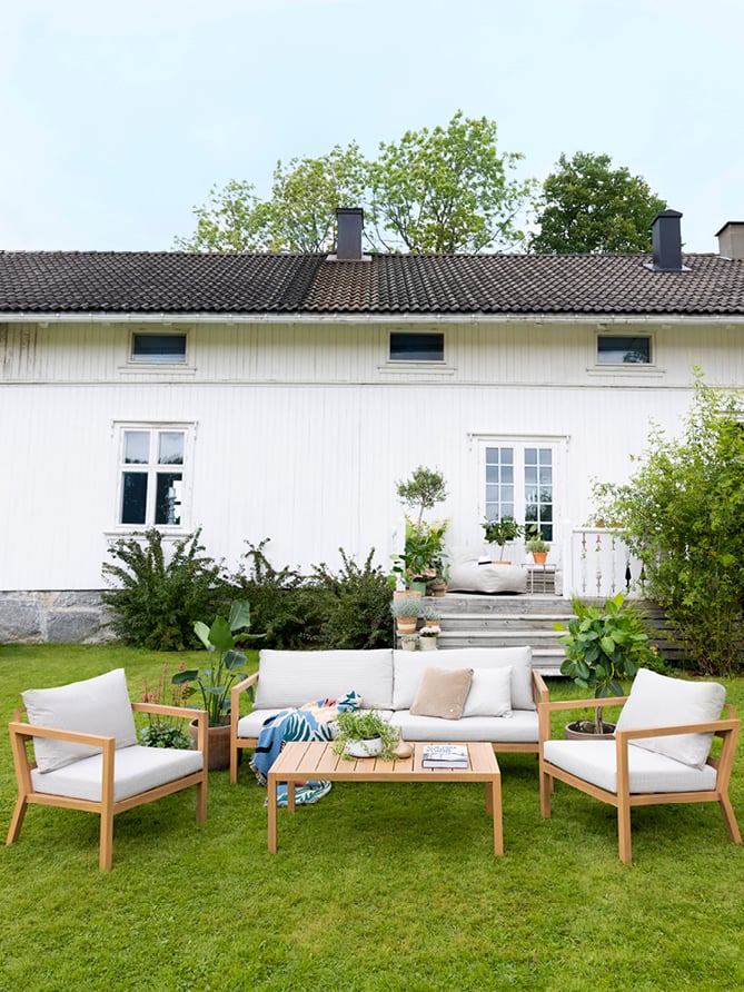 Røst sofaserie i teak på en gressplen foran et hus. 