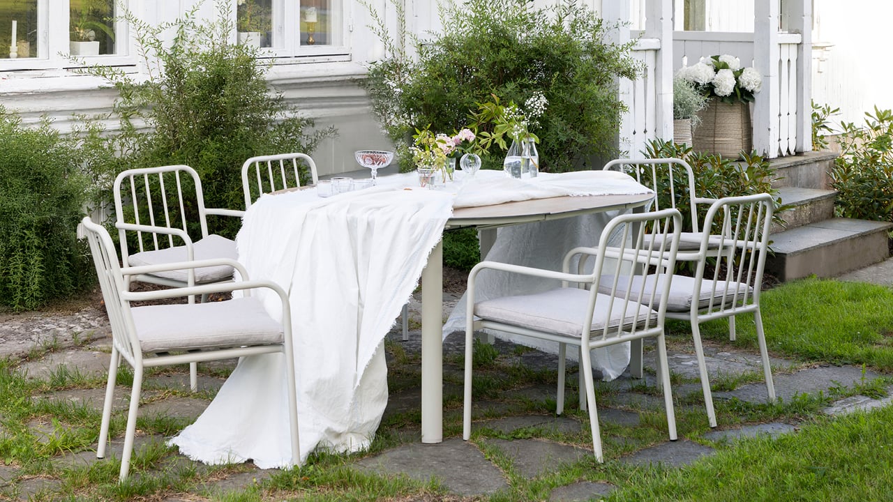 Bohem Brevik stol i kalk med pute rundt Bohem Nesodden bord med hvit duk i en hage.