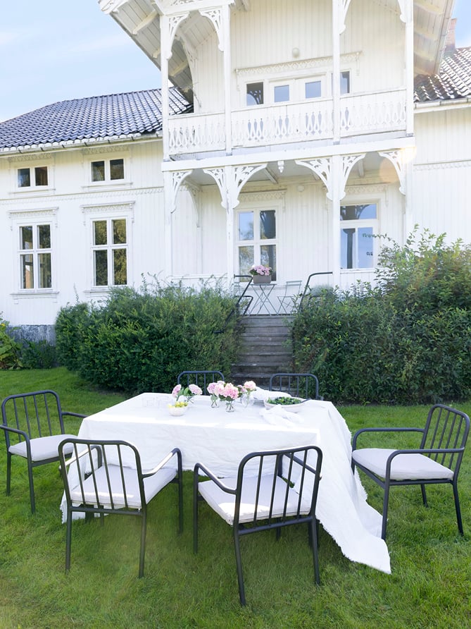Bohem Brevik stol i sort med pute rundt et spisebord med hvit duk i en hage.