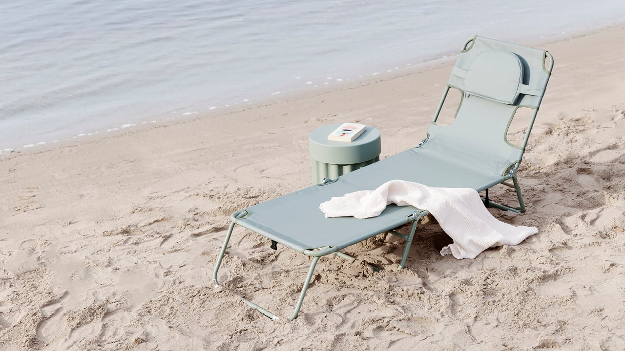 Bohem Scroll solseng i grønn på en strand, med et håndkle på.