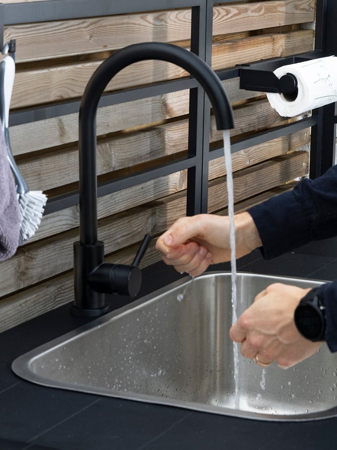 Noen som vasker hendene under kranen på en utendørs vask.