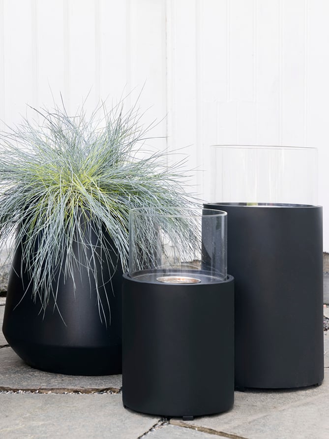 Svart potte med strå i og sorte biolykter utendørs. 