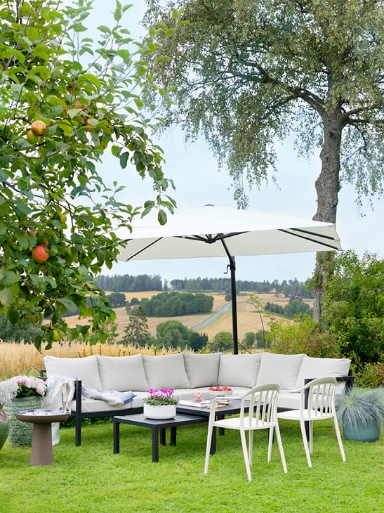 Lys soffa på en gressplen med en flott og stor parasoll over.