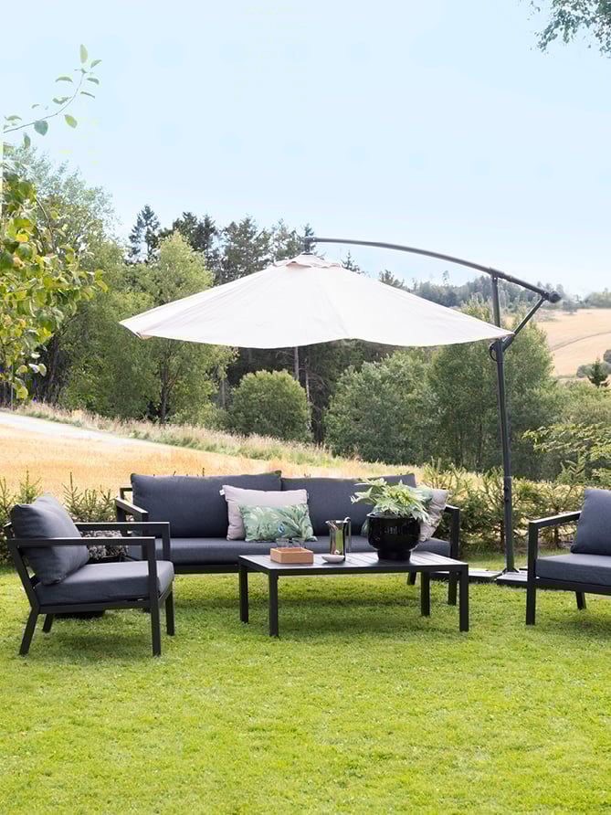 Svart sofa på en gressplen med en fin og stor parasoll over. 