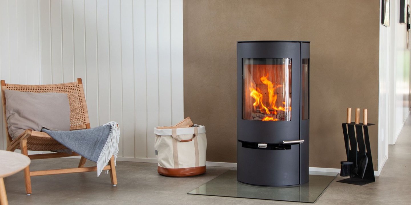 Svart Aduro peis i fyr, ved siden av en stol og en veske med vedkubber i. 