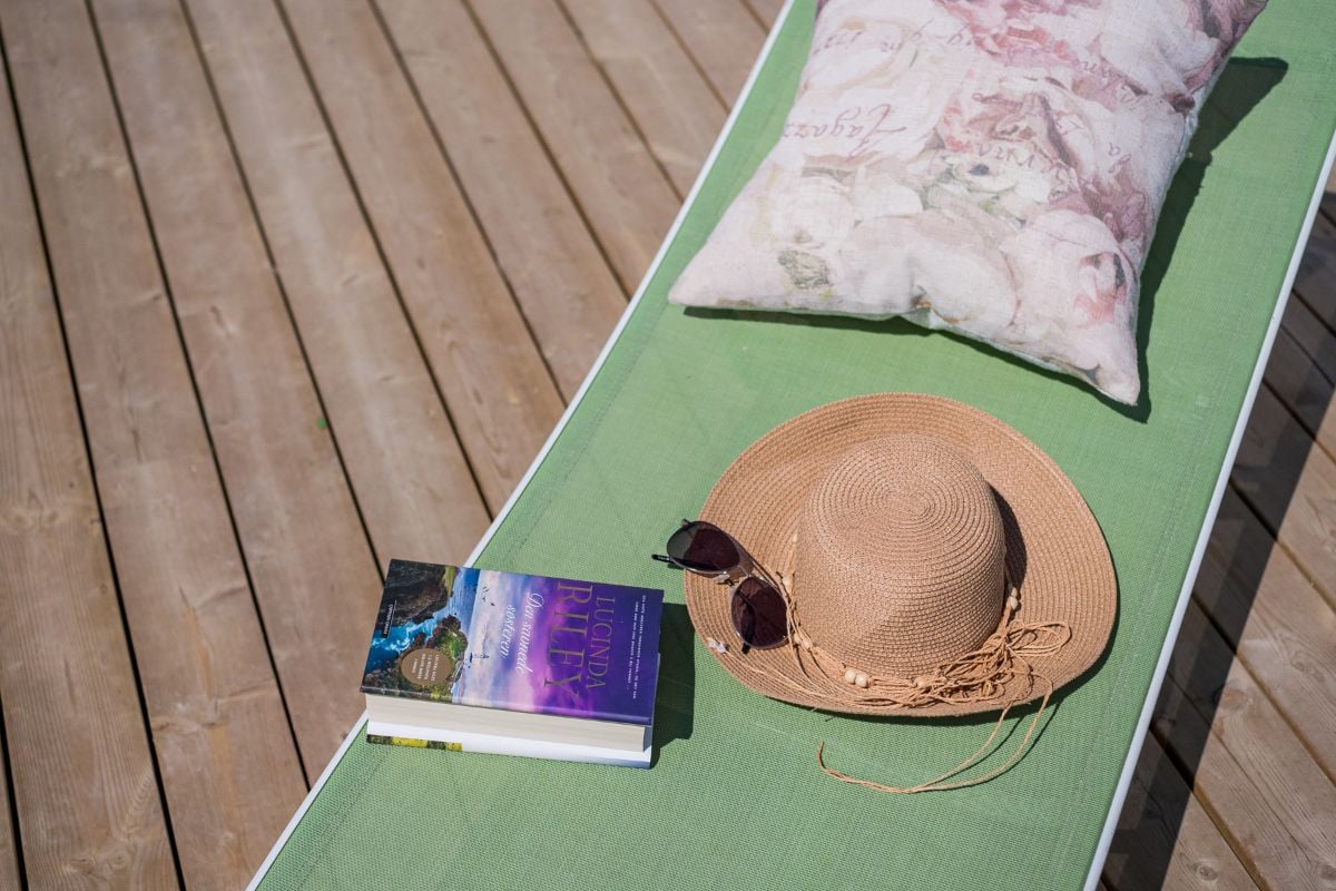 Solhatt, bok og solbriller på en solseng på en terrasse laget av tre