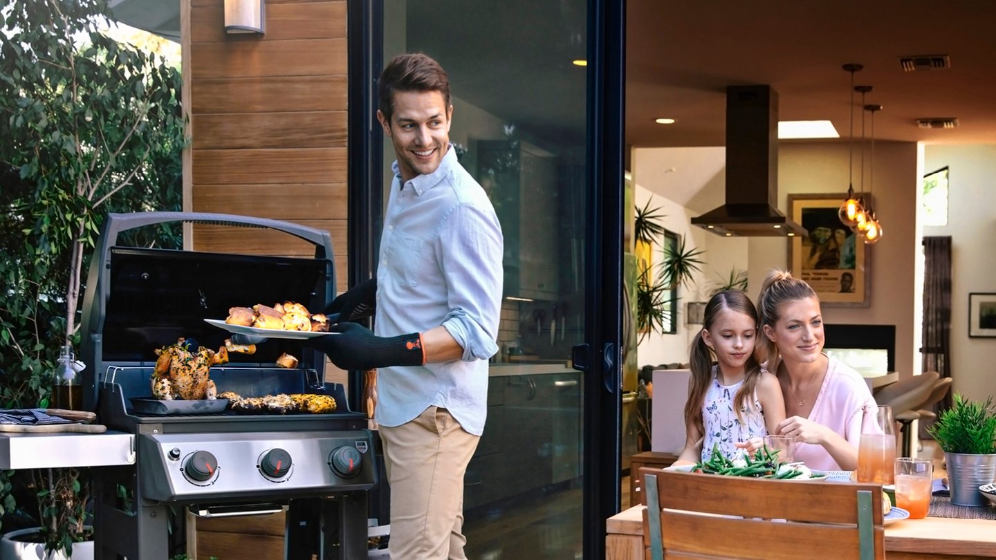 Mann griller og ser på familien på terrasse