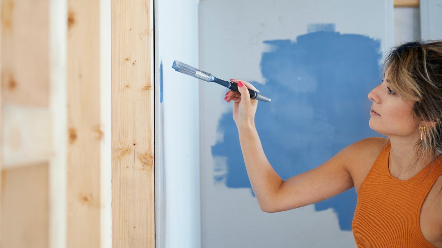 Kvinne maler vegg i blå innendørs