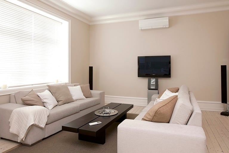 Moderne varmepumpe på en beige vegg i en stue med tv og sofaer.