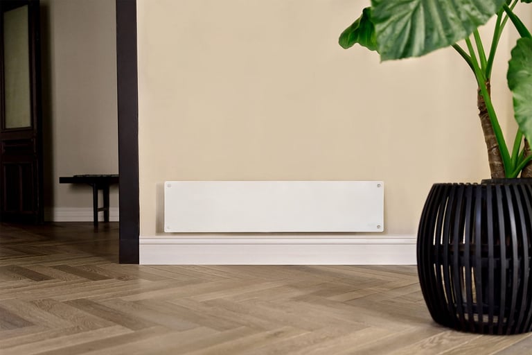 Hvit avlang panelovn med glassfront montert på vegg ved siden av stor grønn plante i stue.