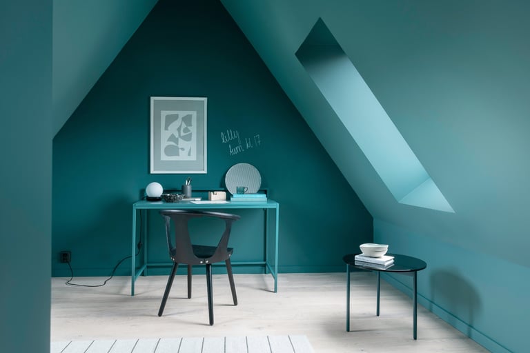 Et rom malt i dyp grønnblå farge, med et skrivebord, stol og dekorasjoner.