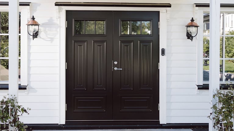 Klassisk inngangsparti med svart dobbel ytterdør og kodelås plassert på veggen ved siden av døren.