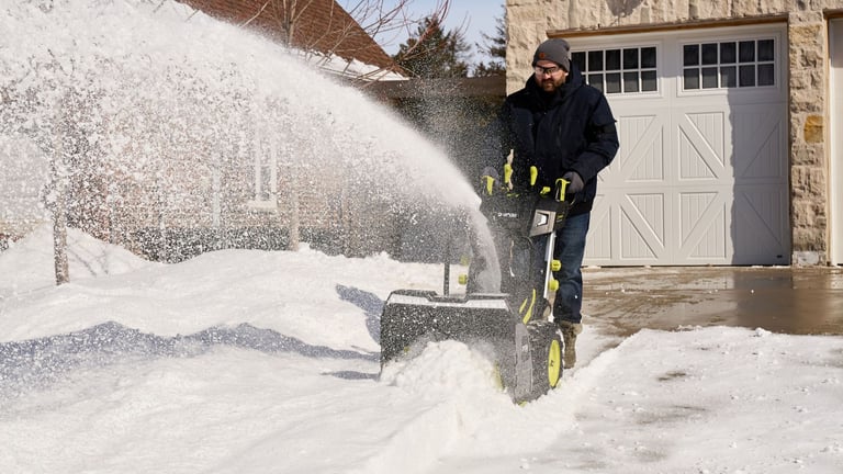 En mann fjerner store snømengder med en kraftig Ryobi snøfreser foran huset.