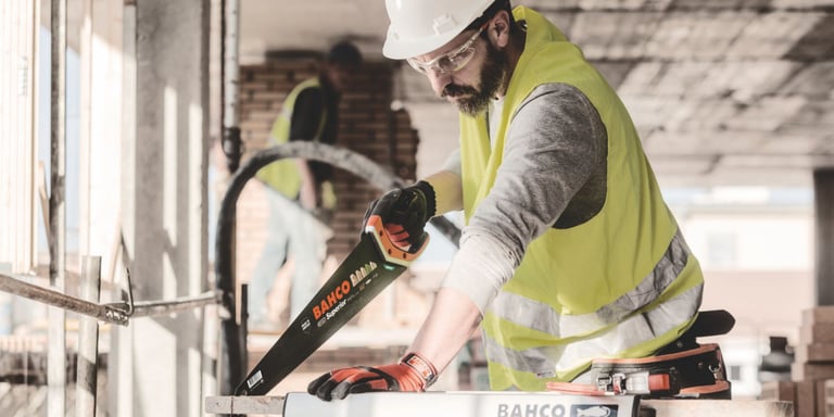 Håndverker med verneutstyr bruker en BAHCO håndsag på byggeplass