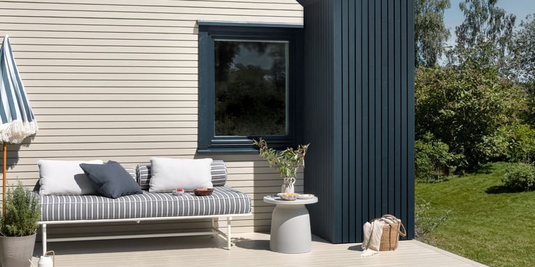 En terrasse i beigefarge på en gressplen. Veggen har blå detaljer. 