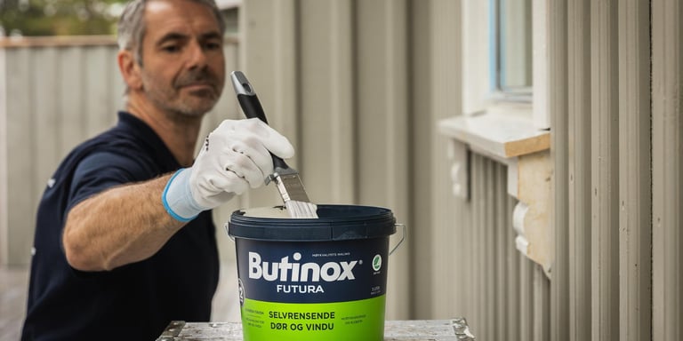 Mann som dypper en pensel i et Butinox Futura malingsspann.