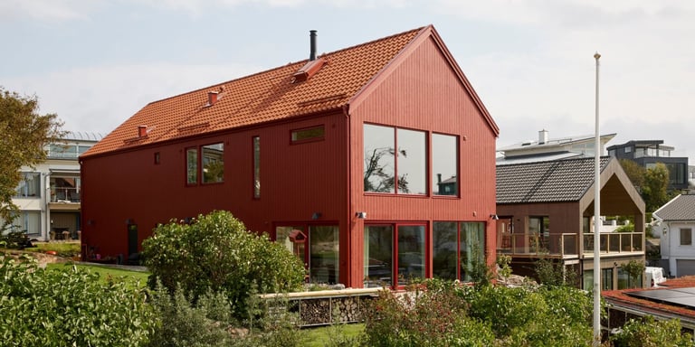 Et rødt hus malt i Drygolin Optimal husmaling. Huset er moderne med store vinduer og er omringet av en grønn og frodig hage.