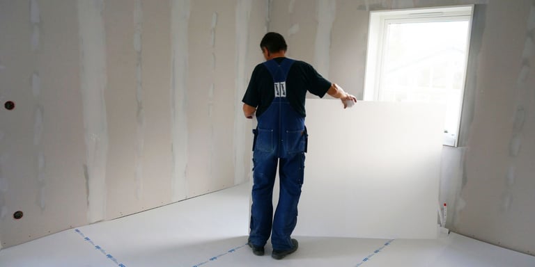 Mann som bærer på beskyttelsesplate, som skal legges på gulvet for oppussing. 