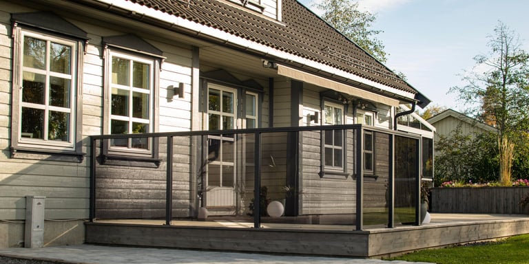 Et brunt hos med hvite vinduer. Det er en terrasse rammet inn med sotet glassrekkverk. 