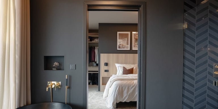 Bad malt i en mørk grå farge kalt Varg fra Gjøco/Infra. Fargen er matt. Du kan se badet, men gjennom døren kan du se et soverom med en beige seng. Man skimter et badekar i venstre hjørne.