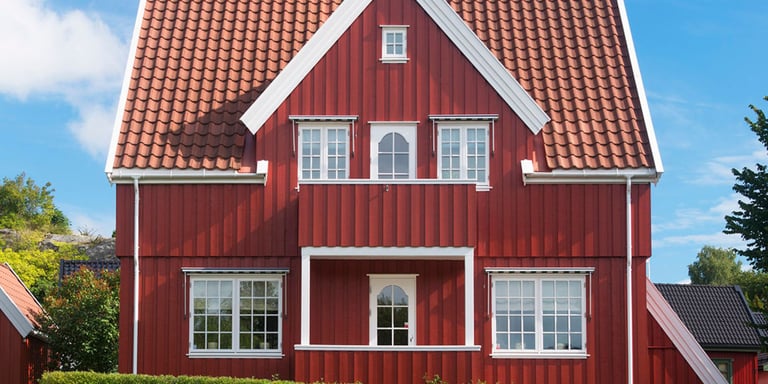 Rødt stort hus med hvit karmer og blå himmel bak