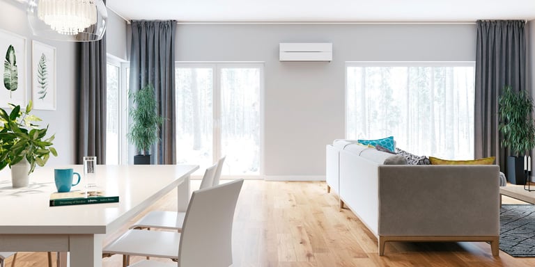 Moderne varmepumpe på en beige vegg i en stue store vinduer og sofa.