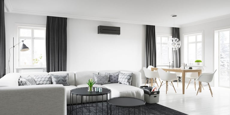 Stue med sofa og svart varmepumpe montert på hvit vegg.