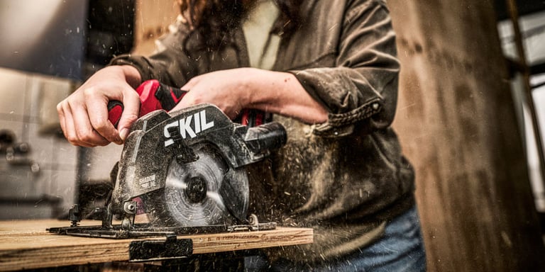 En dame som bruker sirkelsag fra Skil til å skjære i treverk.