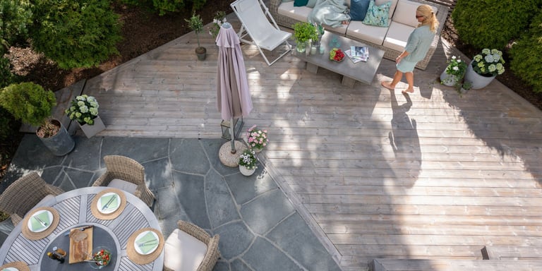 Uteområde av terrassebord og steinheller, med utemøbler i grønne omgivelser