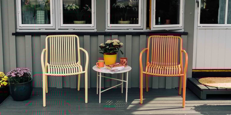 To utestoler i gul og oransje står ute på en terrasse med et lite bord med blomster mellom seg.