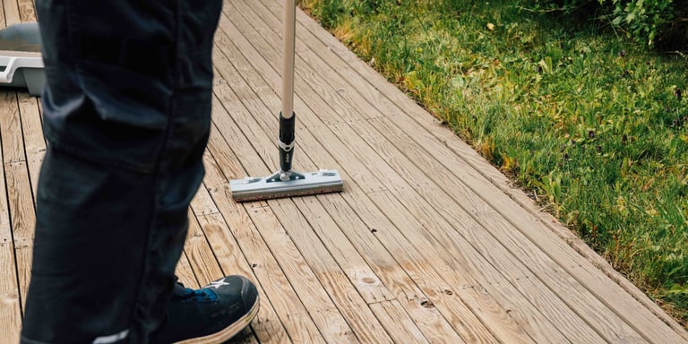 Person som beiser terrassen med kost med skaft. 