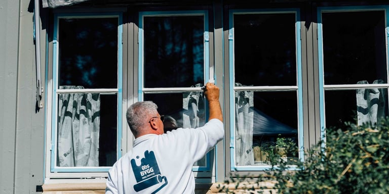 Mann som maler listene ute i en hvit Obs BYGG genser.