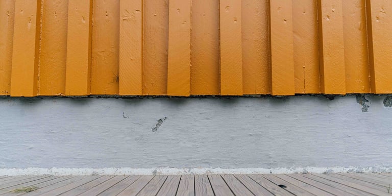 Bilde av en gul husvegg med en grå grunnmur.