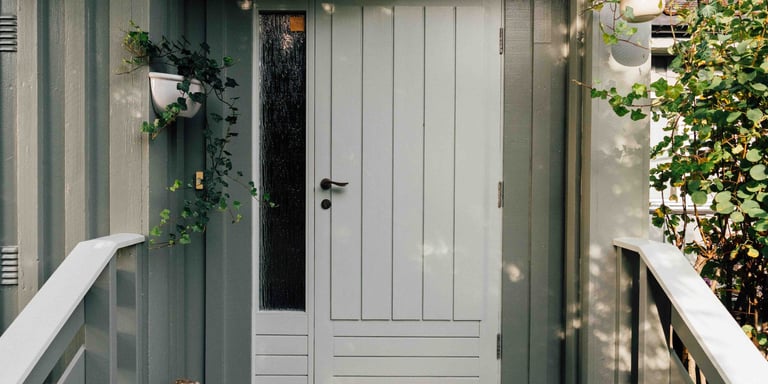 Nymalt hvit ytterdør, med grønne planter rundt på et grått hus